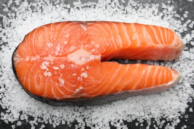 Photo of Fresh raw salmon steak with salt on dark table, above view