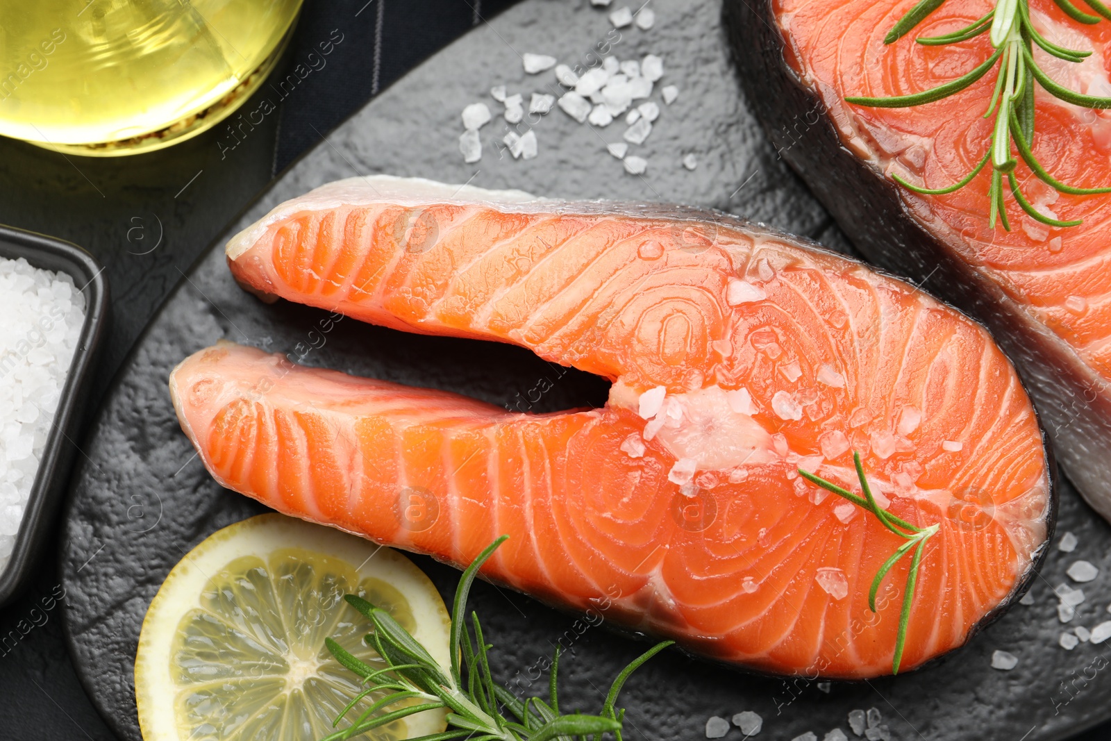 Photo of Fresh raw salmon steaks with salt, lemon and rosemary on dark table, flat lay