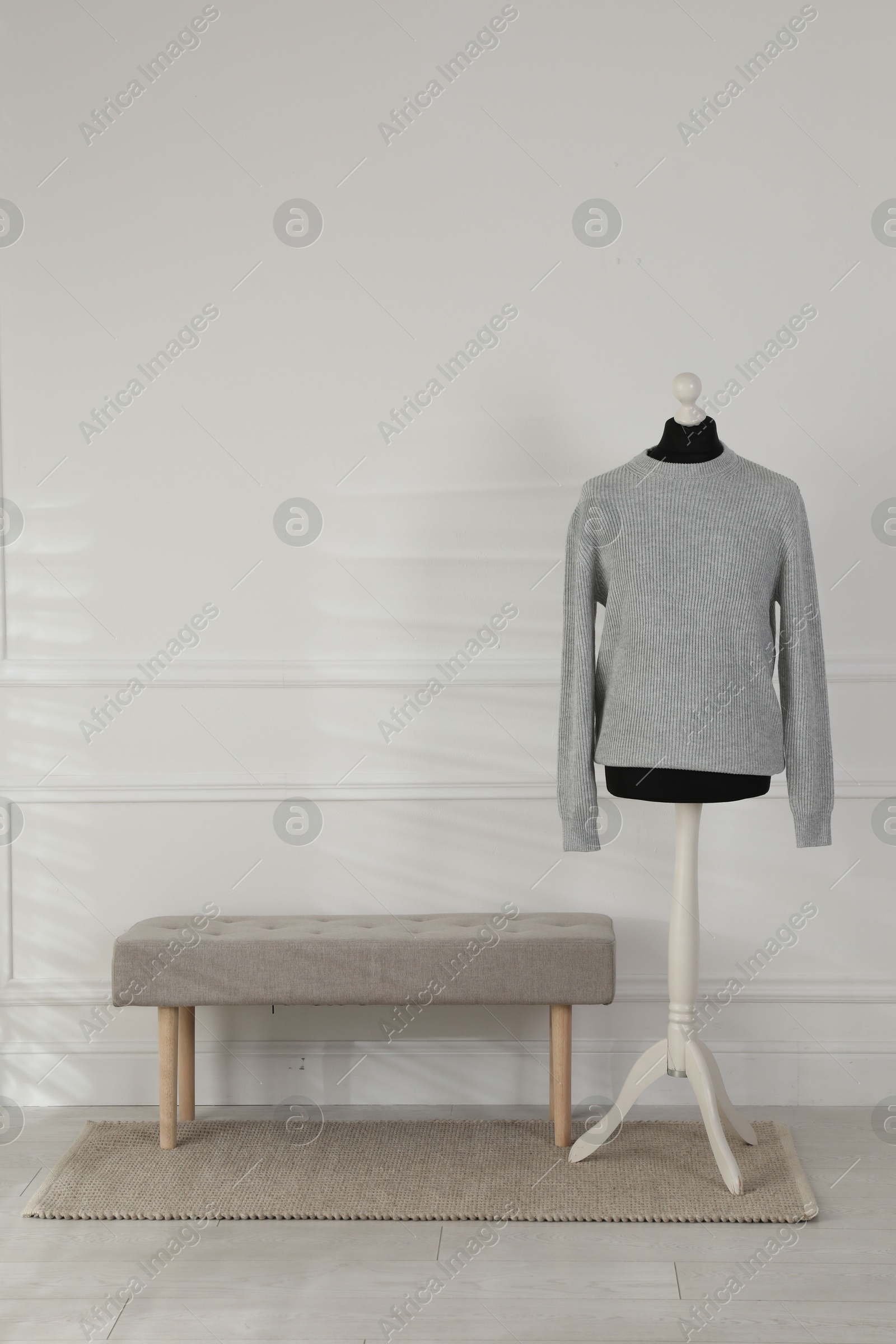 Photo of Female mannequin with sweater and bench near light wall