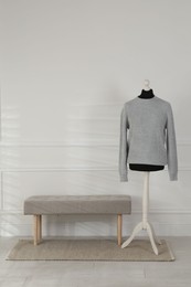 Female mannequin with sweater and bench near light wall