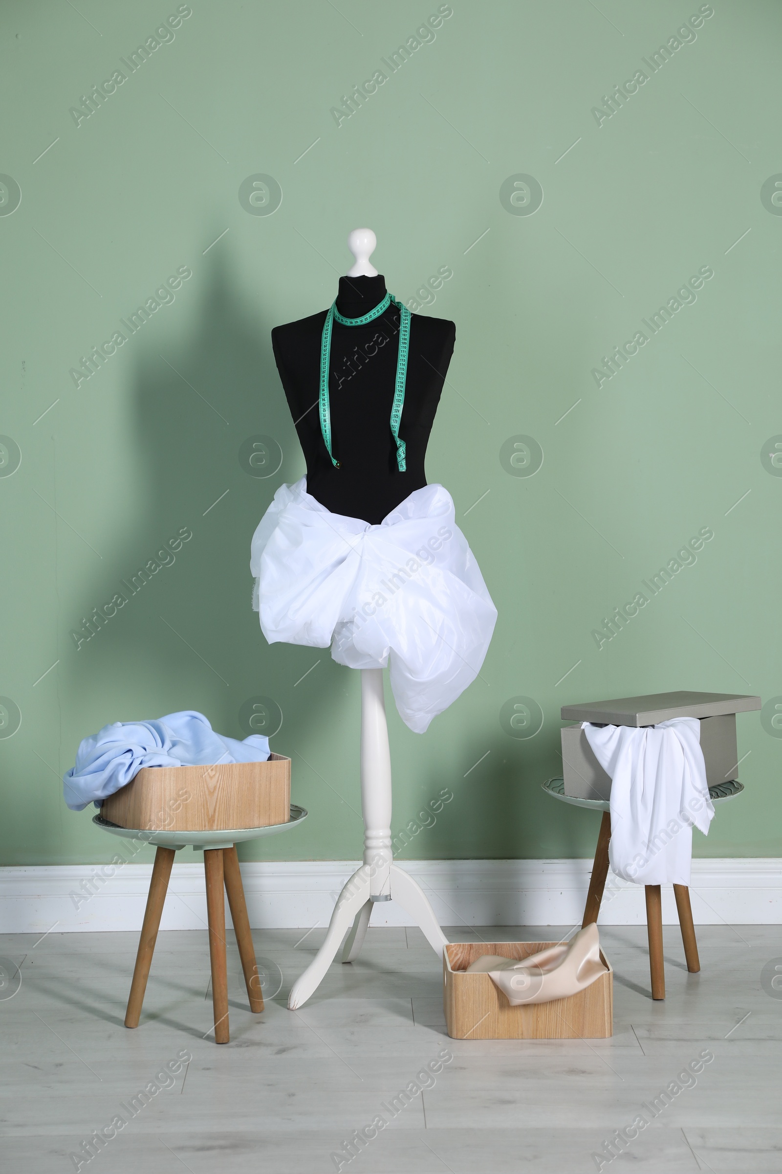 Photo of Female mannequin with fabric, measuring tape and clothes near green wall