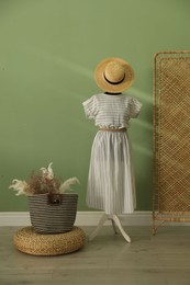 Female mannequin with dress, hat, bag, dry plants and folding screen near green wall