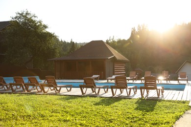 Photo of Outdoor swimming pool, sunbeds and houses near forest on sunny day