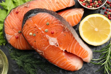 Photo of Fresh raw salmon steaks with spices and products on dark textured table, closeup