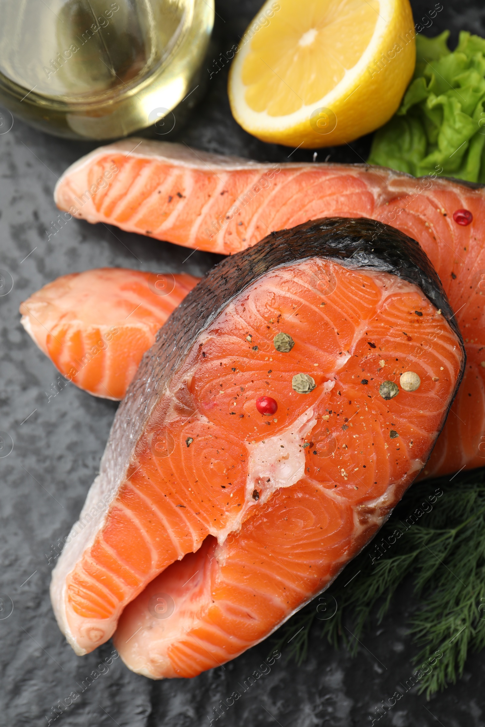 Photo of Fresh raw salmon steaks with spices and products on dark textured table, above view