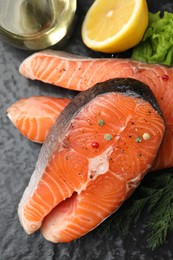 Photo of Fresh raw salmon steaks with spices and products on dark textured table, above view