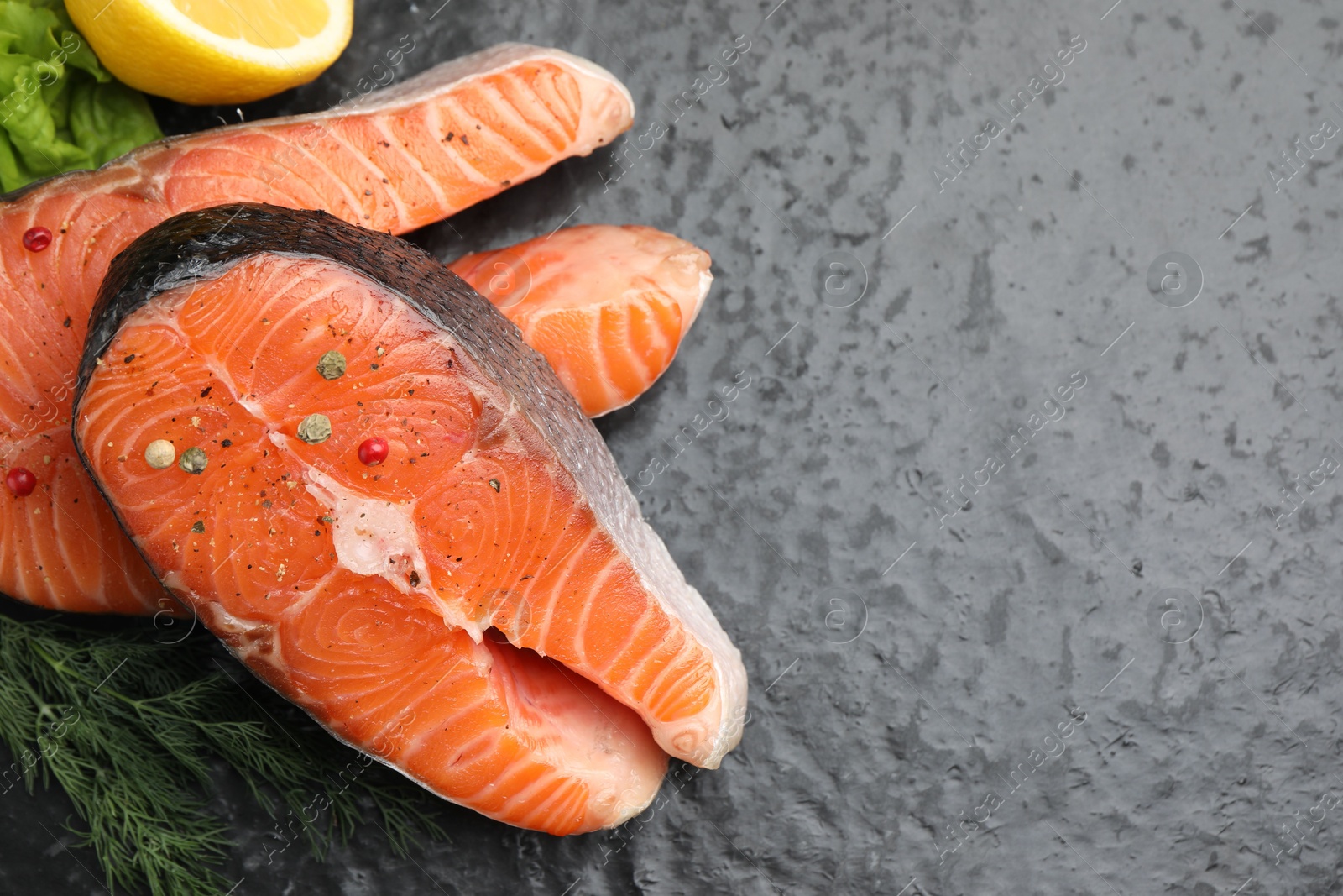 Photo of Fresh raw salmon steaks with spices and dill on dark textured table, above view. Space for text