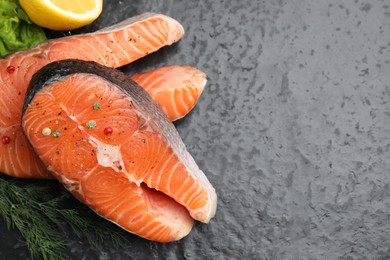 Photo of Fresh raw salmon steaks with spices and dill on dark textured table, above view. Space for text