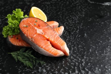 Photo of Fresh raw salmon steaks with spices, lemon, lettuce and dill on dark textured table, closeup. Space for text