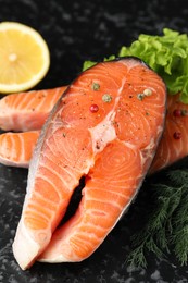 Photo of Fresh raw salmon steaks with spices, lemon, lettuce and dill on dark textured table, closeup