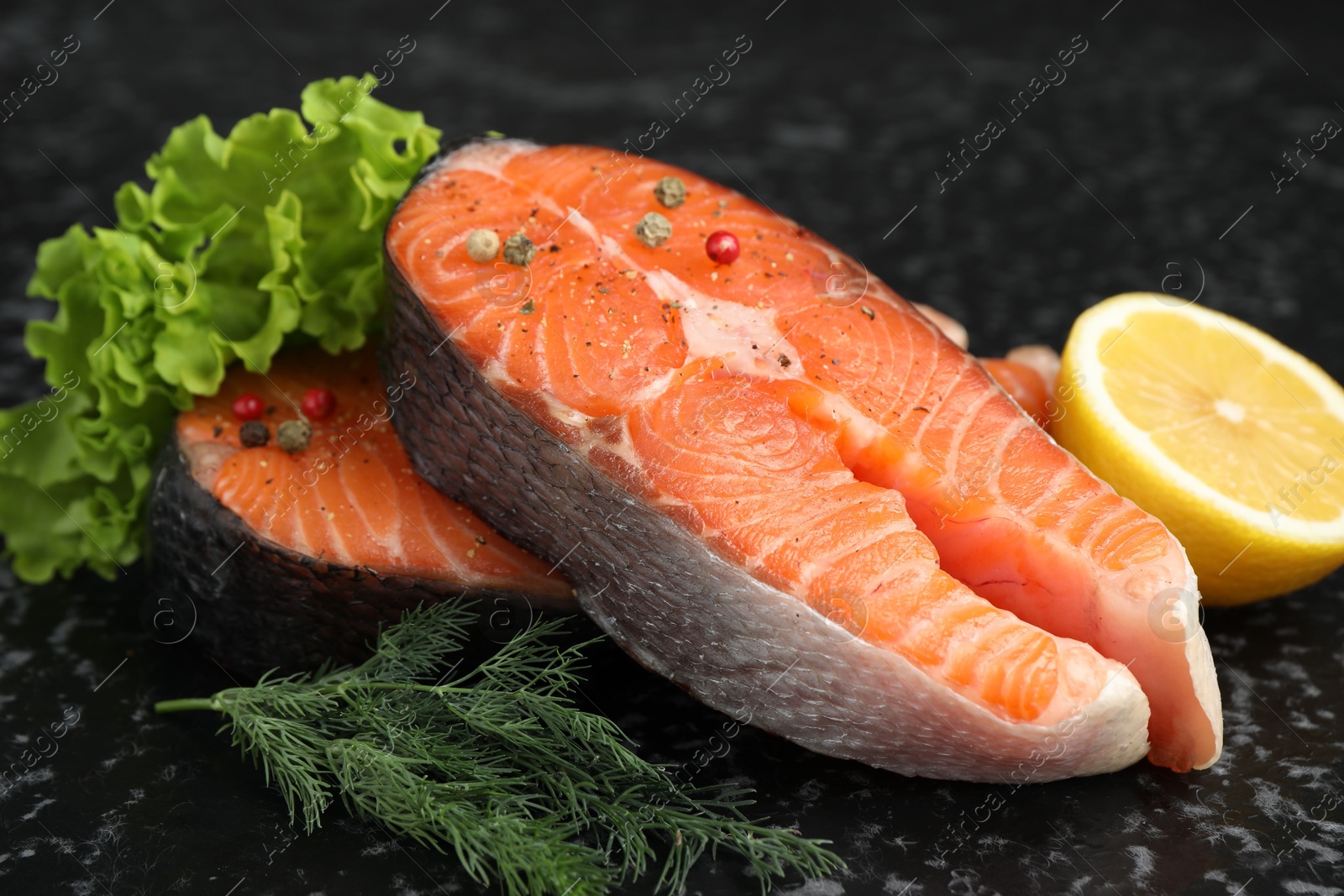 Photo of Fresh raw salmon steaks with spices, lemon, lettuce and dill on dark textured table, closeup