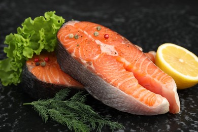 Photo of Fresh raw salmon steaks with spices, lemon, lettuce and dill on dark textured table, closeup