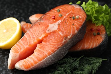 Photo of Fresh raw salmon steaks with spices, lemon, lettuce and dill on dark textured table, closeup