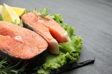 Photo of Fresh raw salmon steaks with spices, lemon, lettuce and rosemary on dark textured table, closeup. Space for text