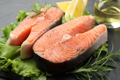 Photo of Fresh raw salmon steaks with spices, lettuce and rosemary on dark table, closeup