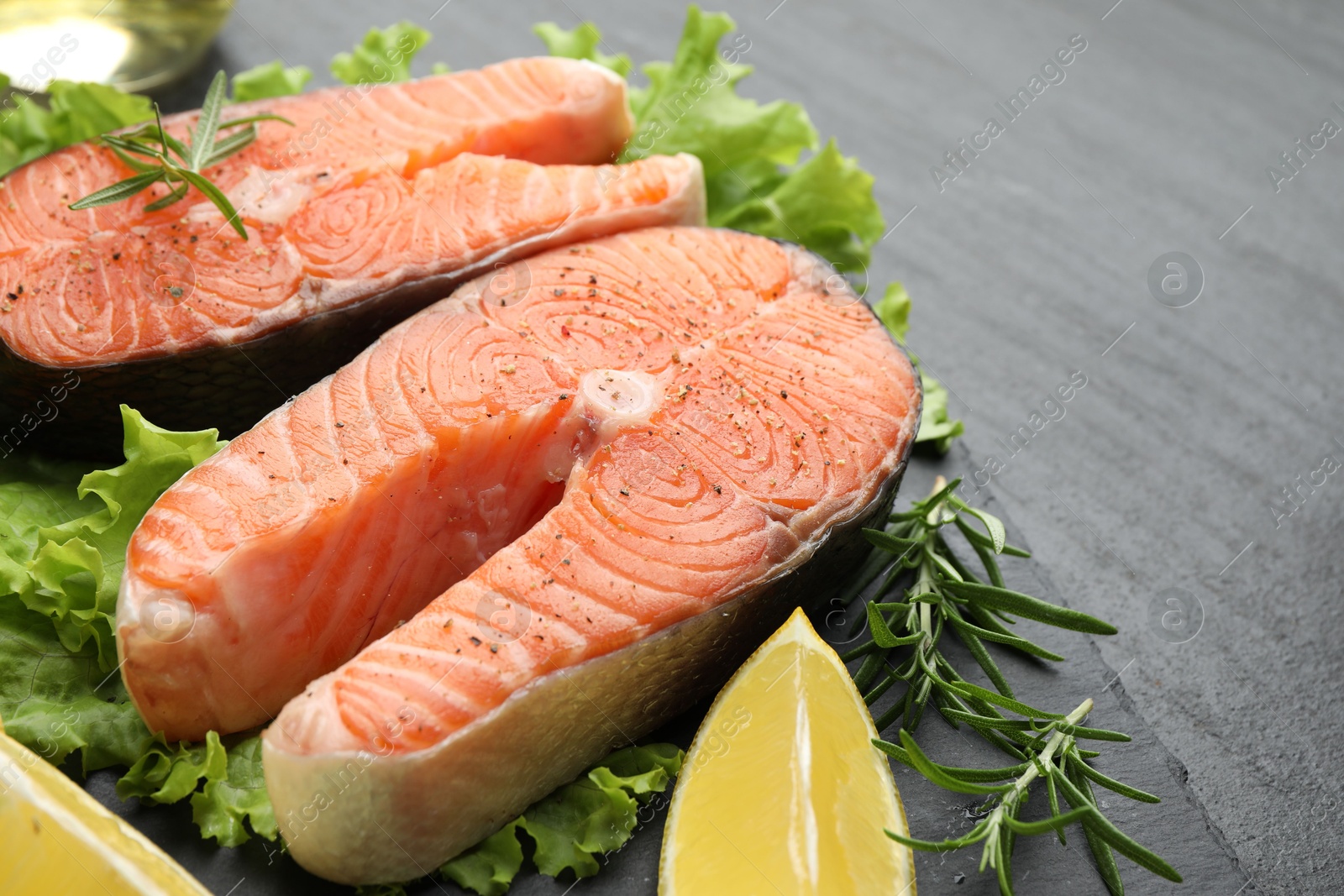 Photo of Fresh raw salmon steaks with spices, lemon, lettuce and rosemary on dark textured table, closeup