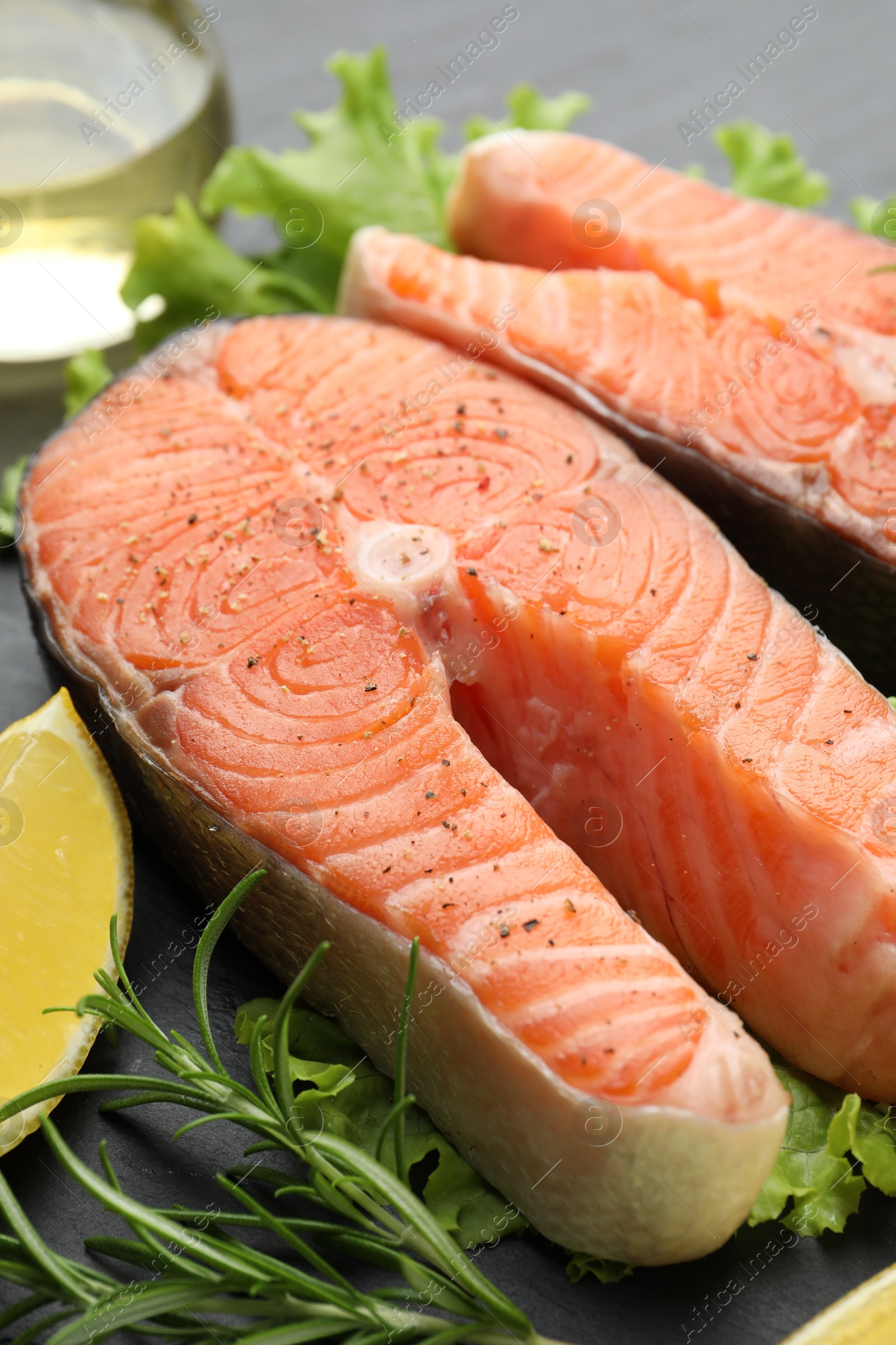 Photo of Fresh raw salmon steaks with spices, lemon and rosemary on dark table, closeup