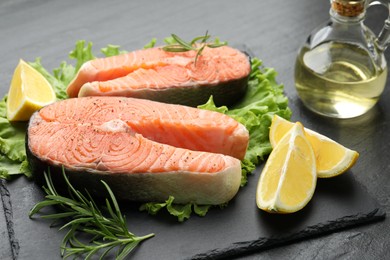 Photo of Fresh raw salmon steaks with spices, lemon, lettuce and rosemary on dark textured table, closeup