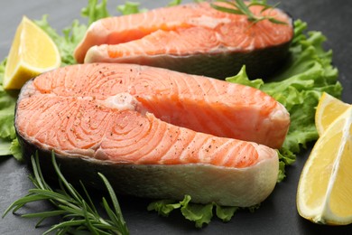 Photo of Fresh raw salmon steaks with spices, lemon, lettuce and rosemary on dark table, closeup