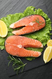 Photo of Fresh raw salmon steaks with spices, lemon, lettuce and rosemary on dark textured table, top view