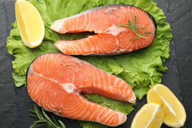 Photo of Fresh raw salmon steaks with spices, lemon, lettuce and rosemary on dark textured table, top view