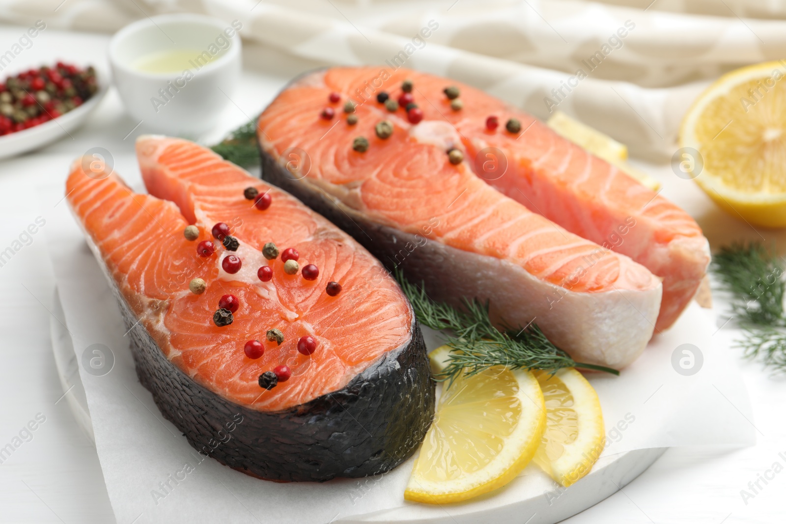 Photo of Fresh raw salmon steaks with peppercorns, lemon and dill on white table, closeup