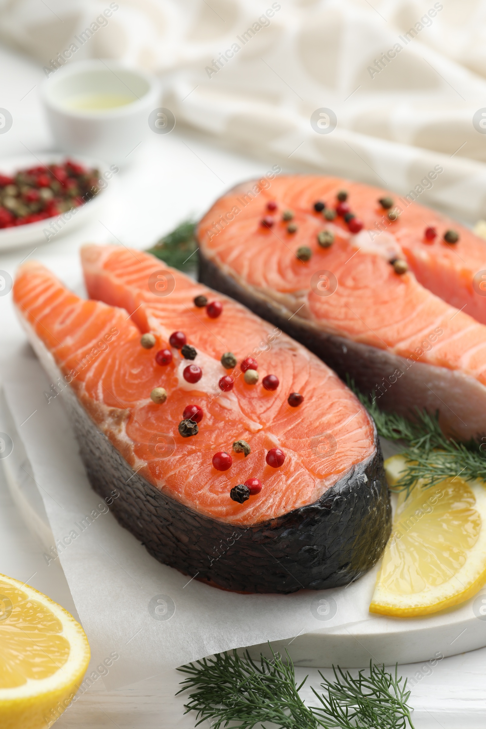 Photo of Fresh raw salmon steaks with peppercorns, lemon and dill on white table, closeup