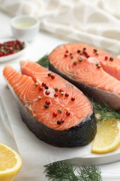 Photo of Fresh raw salmon steaks with peppercorns, lemon and dill on white table, closeup