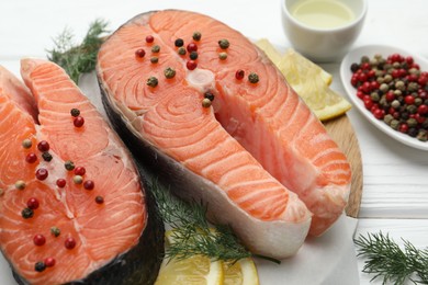 Photo of Fresh raw salmon steaks with peppercorns, lemon and dill on white wooden table, closeup