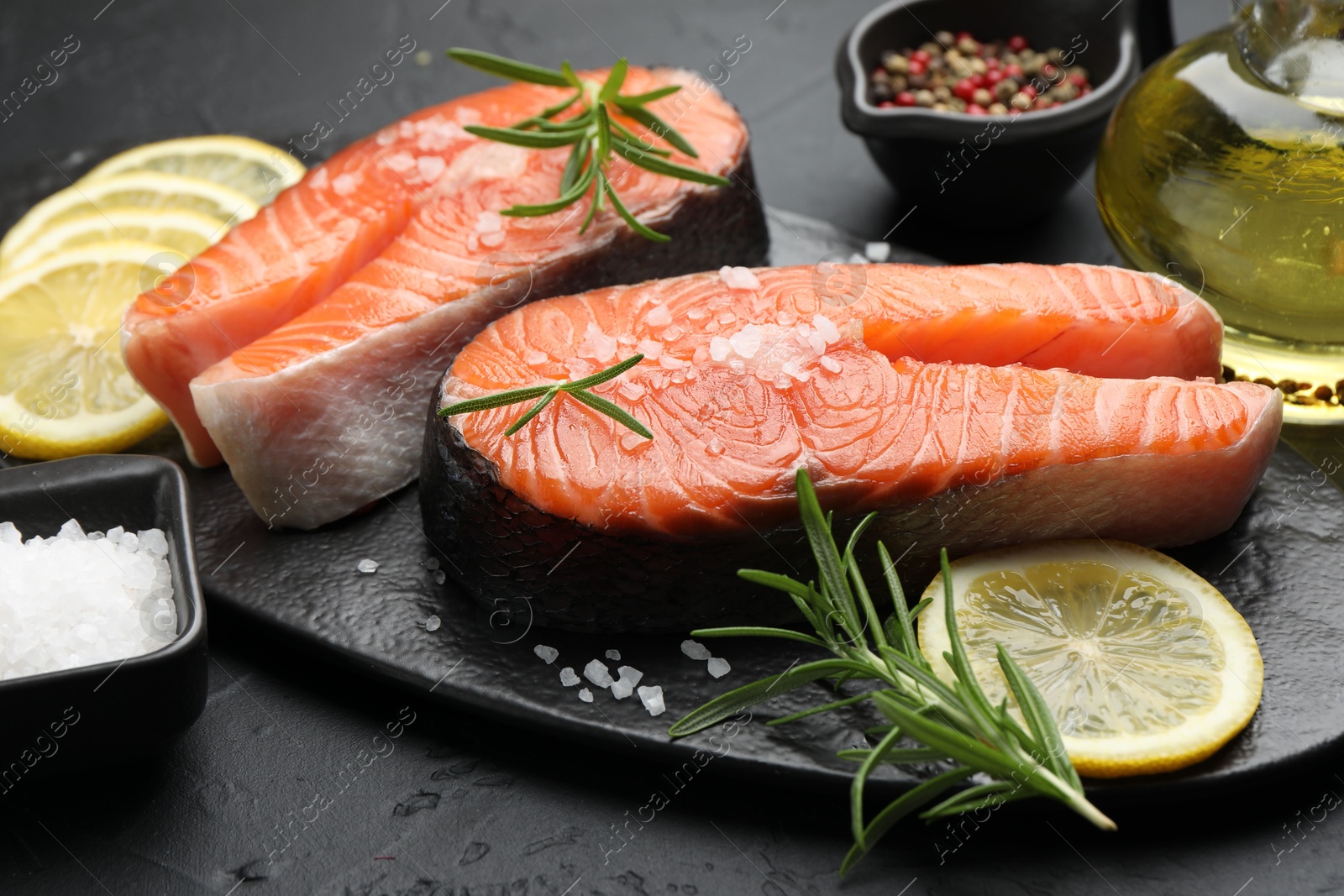 Photo of Fresh raw salmon steaks with salt, lemon and rosemary on dark textured table, closeup