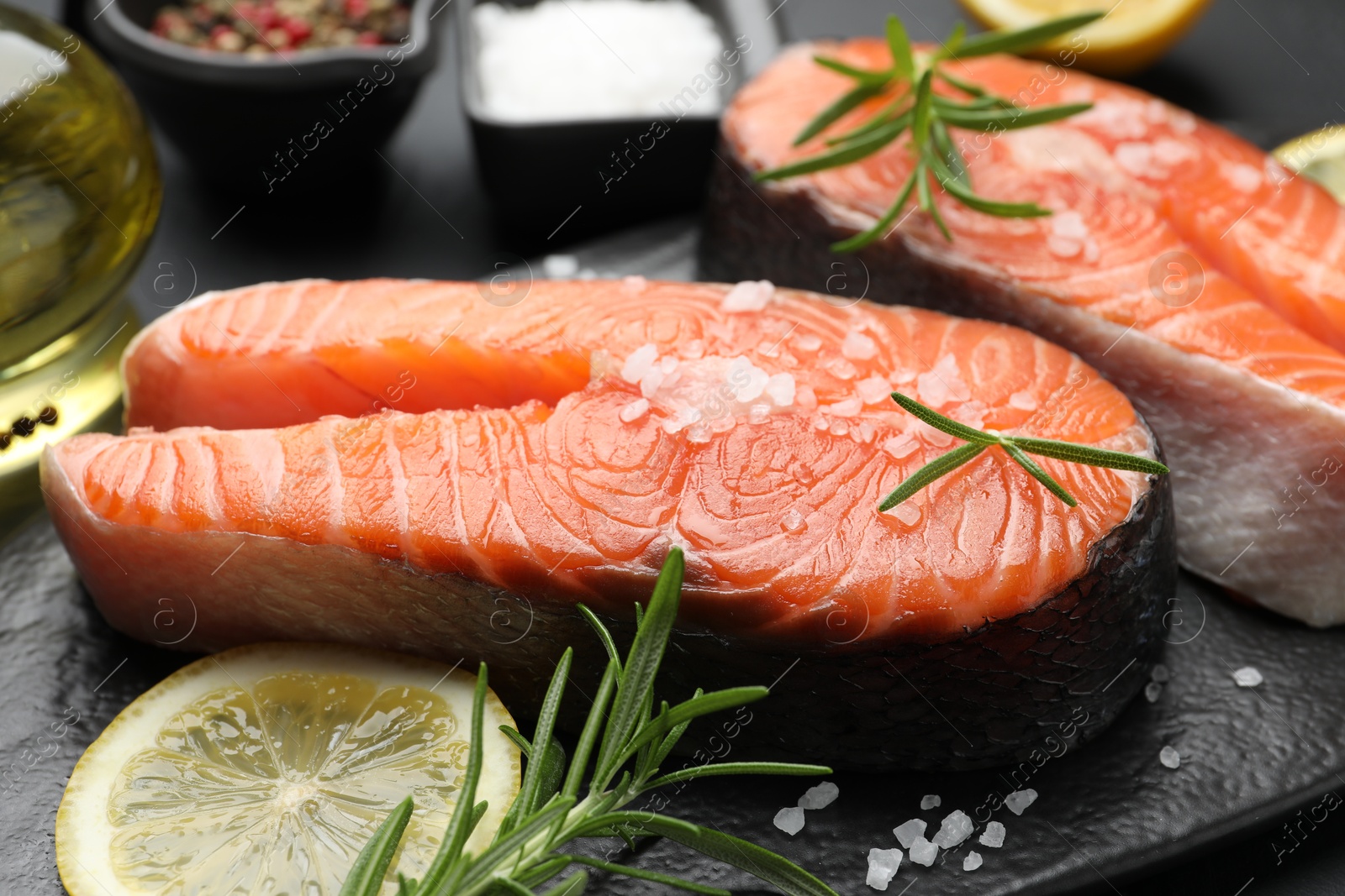 Photo of Fresh raw salmon steaks with salt, lemon and rosemary on dark table, closeup