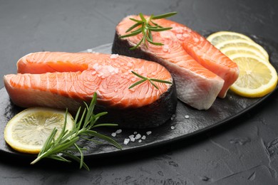 Photo of Fresh raw salmon steaks with salt, lemon and rosemary on dark textured table, closeup