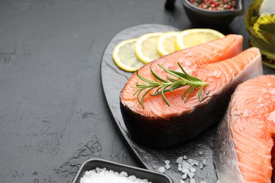 Photo of Fresh raw salmon steaks with salt, lemon and rosemary on dark textured table, closeup. Space for text