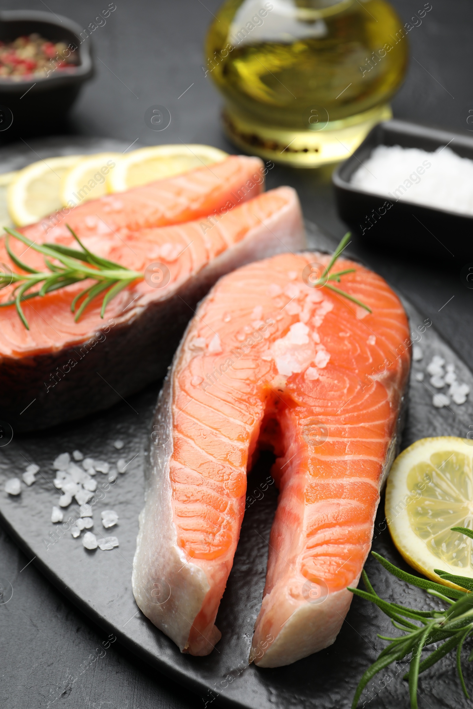 Photo of Fresh raw salmon steaks with salt, lemon and rosemary on dark textured table, closeup