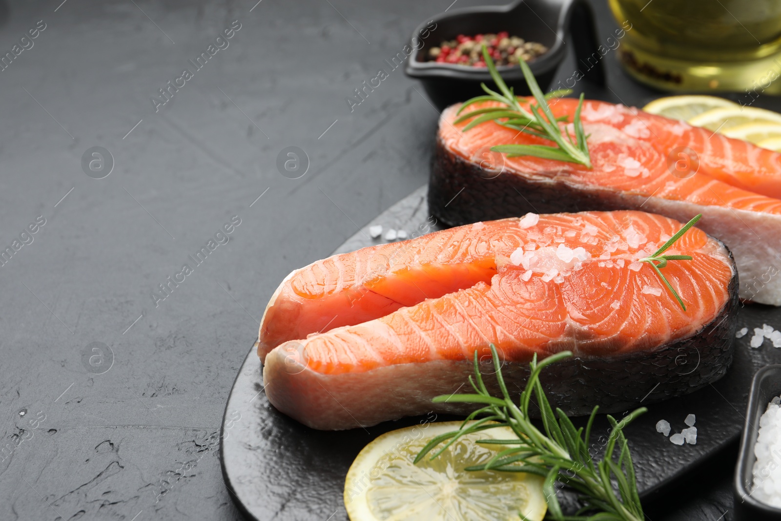 Photo of Fresh raw salmon steaks with salt, lemon and rosemary on dark textured table, closeup. Space for text