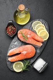 Photo of Fresh raw salmon steaks with salt, lemon, oil, peppercorns and rosemary on dark textured table, flat lay