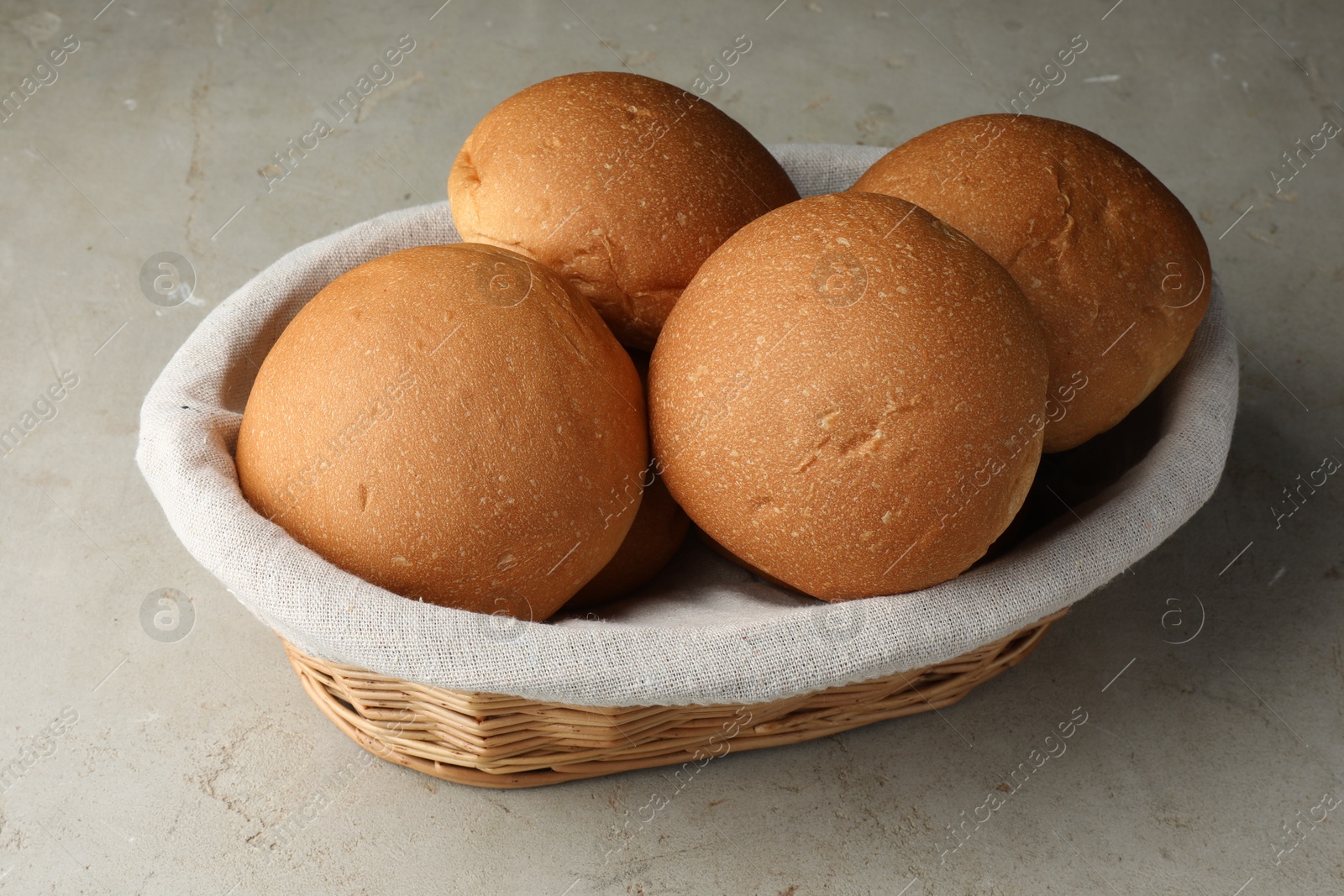 Photo of Fresh tasty buns in basket on grey table, closeup