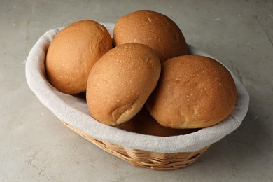 Fresh tasty buns in basket on grey table, closeup