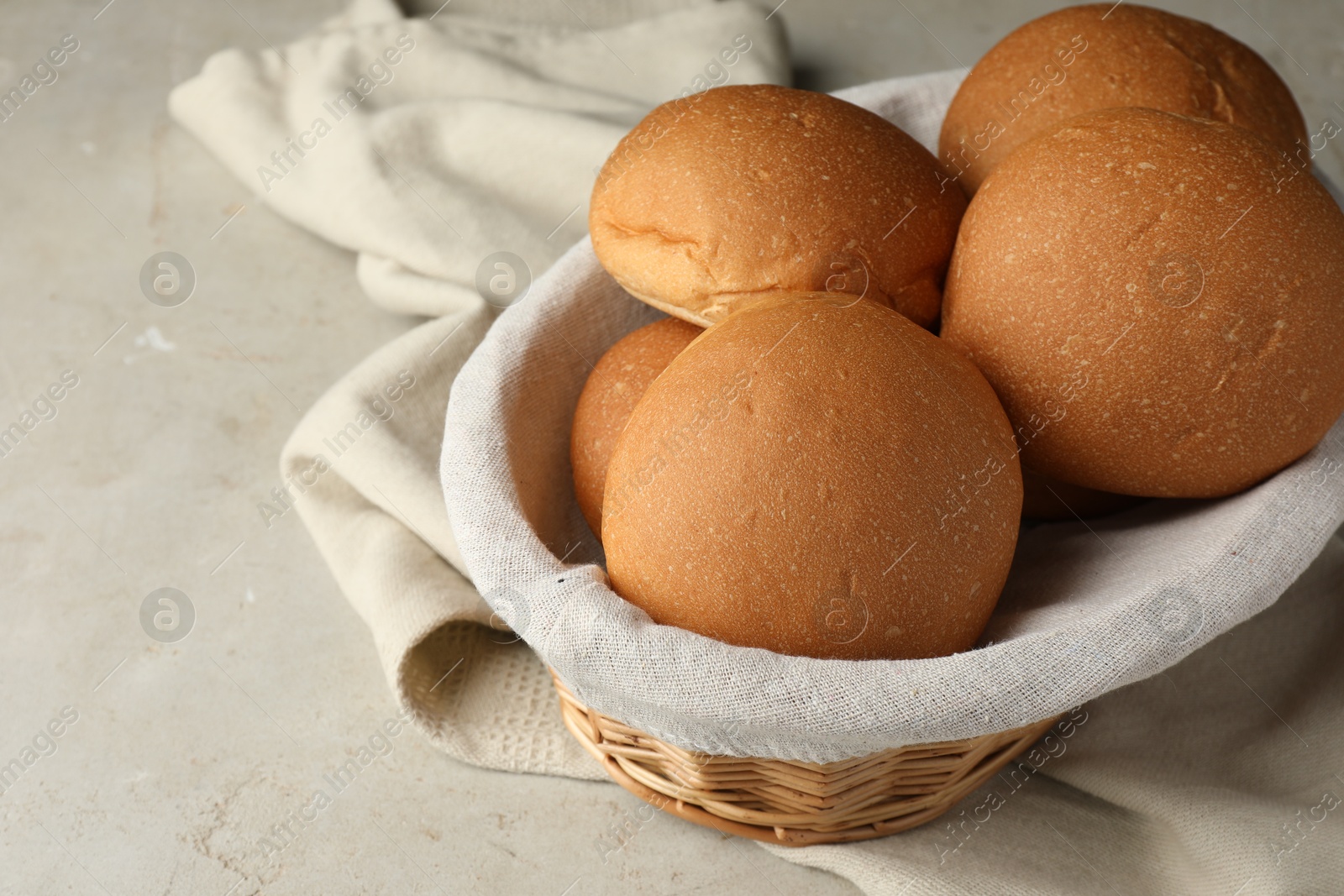 Photo of Fresh tasty buns in basket on grey table, closeup