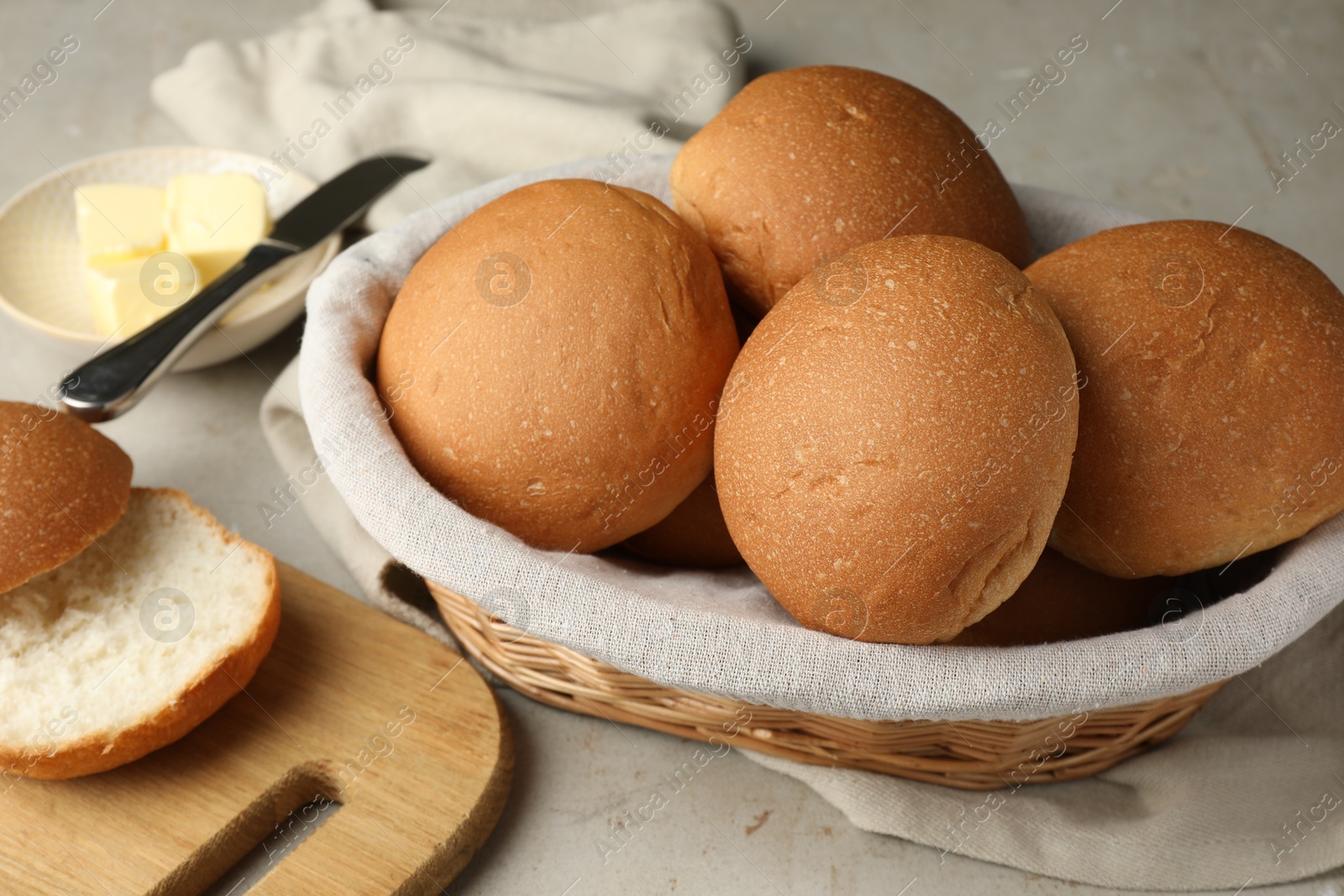 Photo of Fresh tasty buns in basket and butter on grey table, closeup