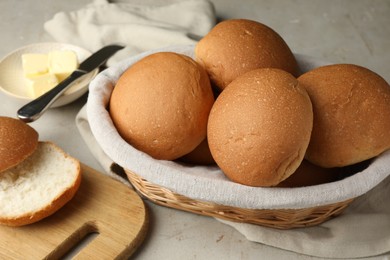 Fresh tasty buns in basket and butter on grey table, closeup