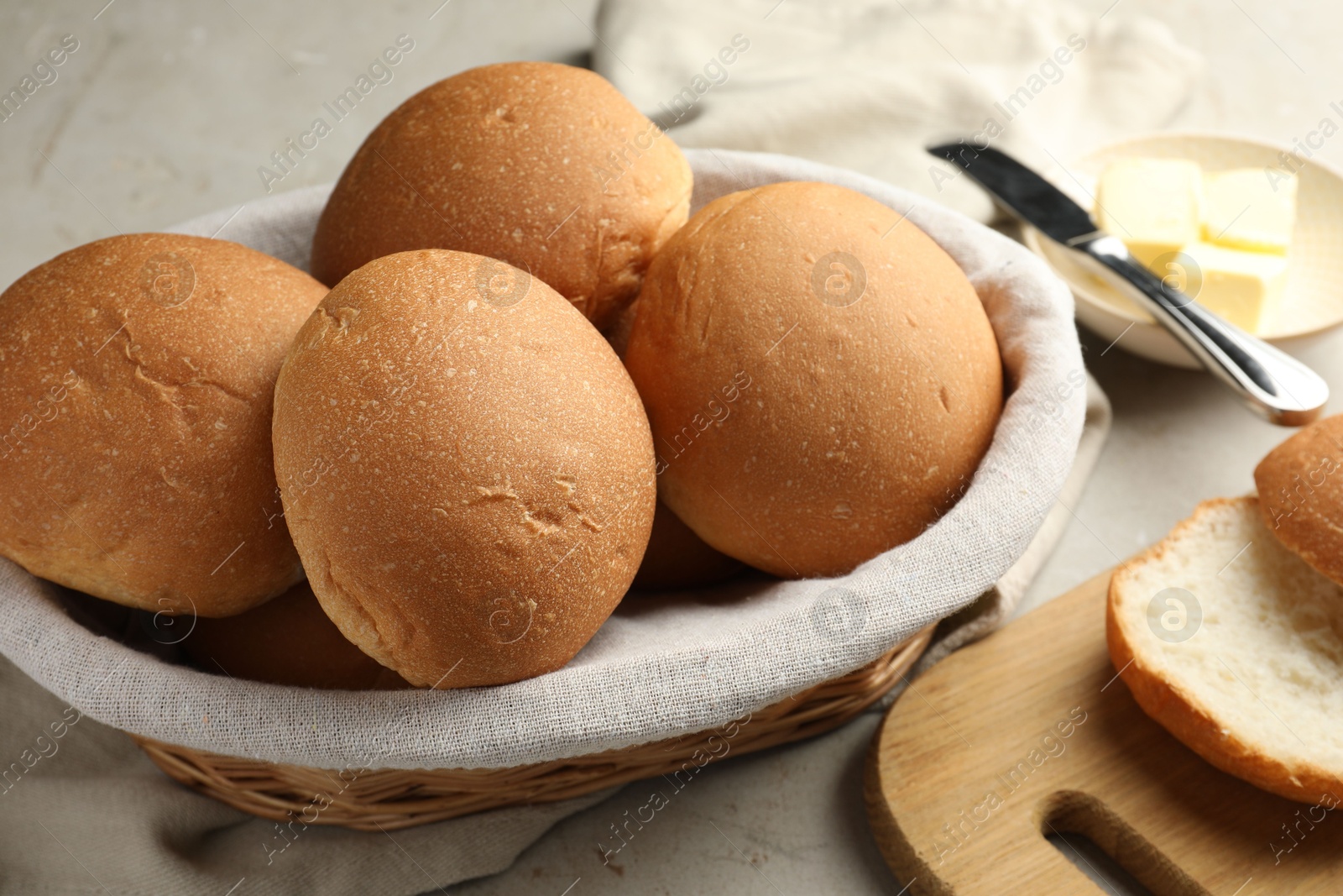 Photo of Fresh tasty buns in basket and butter on grey table, closeup