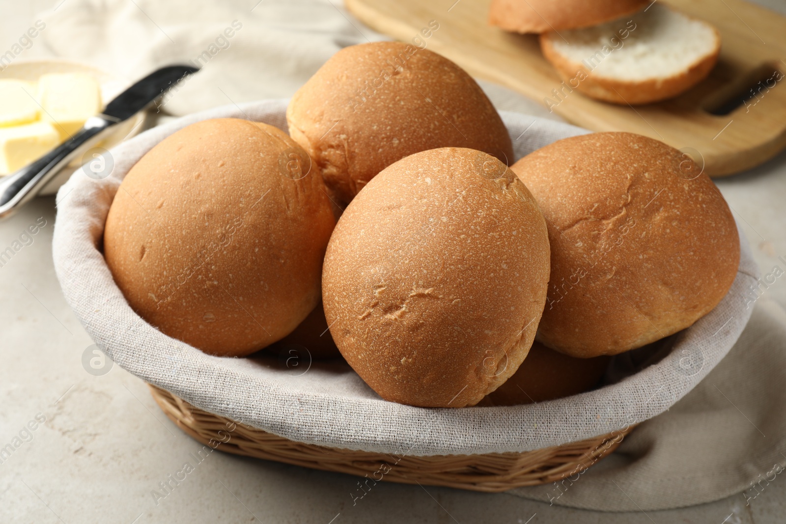 Photo of Fresh tasty buns in basket and butter on grey table, closeup