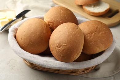 Fresh tasty buns in basket and butter on grey table, closeup