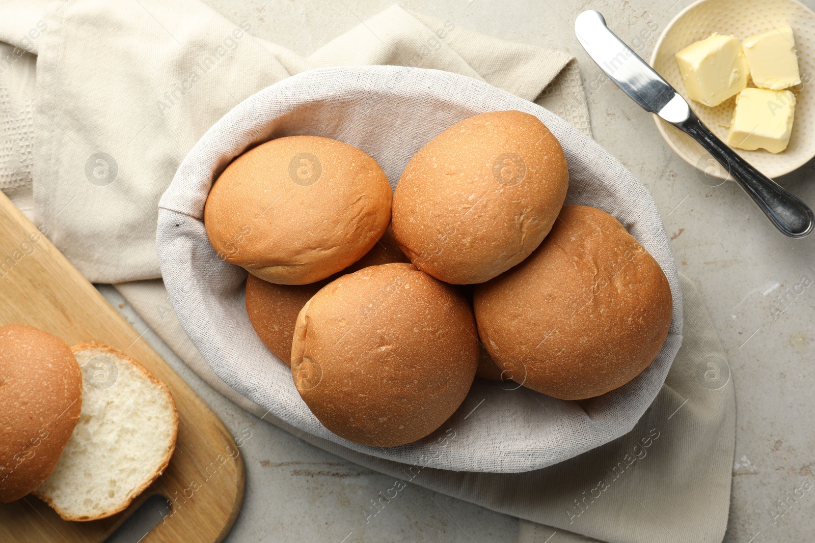 Photo of Fresh tasty buns in basket and butter on grey table, top view