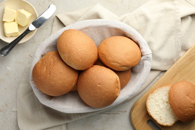 Photo of Fresh tasty buns in basket and butter on grey table, top view