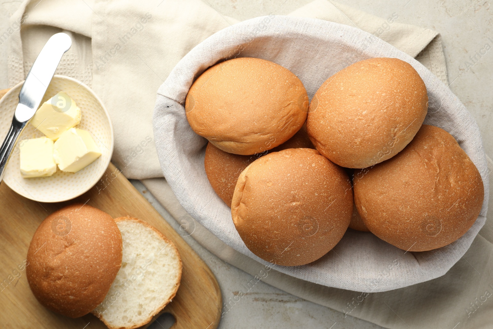 Photo of Fresh tasty buns in basket and butter on grey table, top view