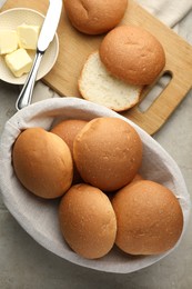 Photo of Fresh tasty buns in basket and butter on grey table, top view