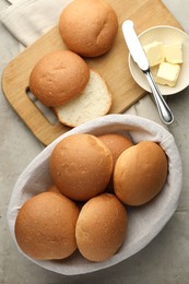 Photo of Fresh tasty buns in basket and butter on grey table, top view