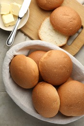 Photo of Fresh tasty buns in basket and butter on grey table, top view